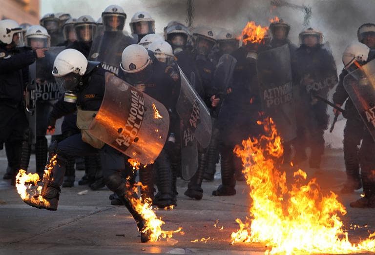 A riot police officers tries to extinguish flames from a petrol bomb thrown by protesters outside the Greek parliament, Athens, Sunday, Feb. 12, 2012. Tens of thousands of protesters gathered in the square outside Parliament. A few hundred anarchists started to throw bottles and firebombs at police, who responded with tear gas and stun grenades. (AP Photo/Thanassis Stavrakis)