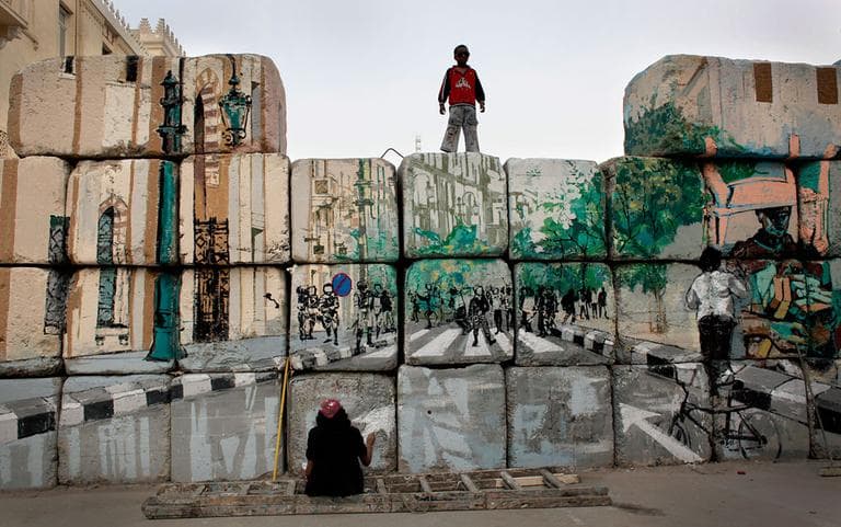 In this Tuesday, March 13, 2012 photo, a boy watches an Egyptian female artist and activist at work on the &quot;No Walls Street&quot; during the graffiti campaign to paint a reproduction of the streets behind them and targeted the concrete blocks walls in downtown Cairo, Egypt. After Egypt's ruling military sealed off streets around Cairo's Tahrir Square with walls of imposing concrete blocks, a group of artists decided to reopen the avenues on their own, in the public imagination, at least. (AP Photo/Nasser Nasser)