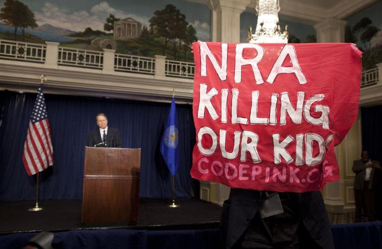 A protester holds up a sign as National Rifle Association executive vice president Wayne LaPierre speaks during a news conference Friday.  (Evan Vucci/AP)