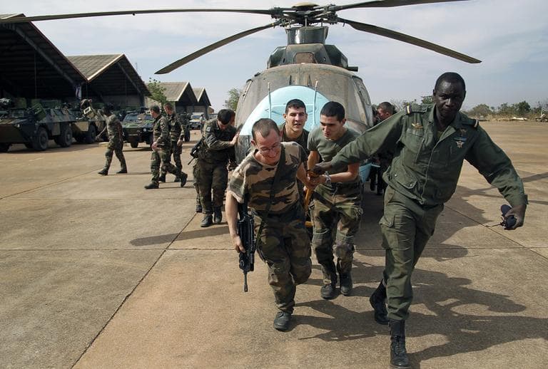 Malian soldiers helped by French troops, move a broken helicopter out a hangar to make room for more incoming troops  at Bamako's airport on Tuesday. French forces led an all-night aerial bombing campaign Tuesday to wrest control of a small Malian town from armed Islamist extremists who seized the area, including its strategic military camp. (Jerome Delay/AP)