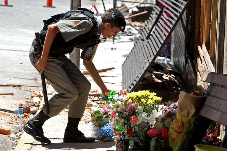 A police officer places flowers outside the Kiss nightclub that were brought by mourners in memory of those who died due to a fire at the club in Santa Maria, Brazil, on Monday. (Nabor Goulart/AP)