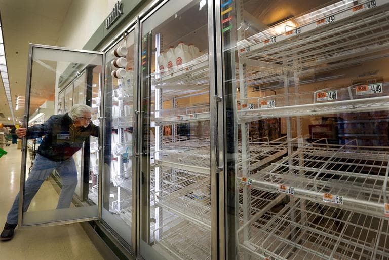 Jack Percoco, of Cambridge, reaches into depleted shelves for milk at a supermarket in Somerville Friday. (Elise Amendola/AP)