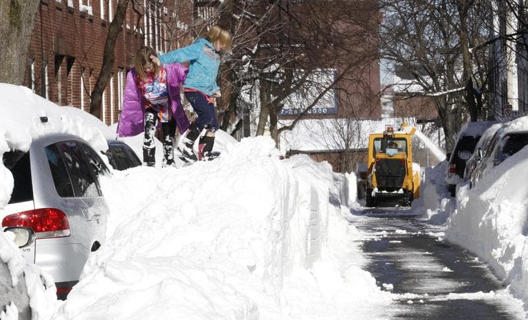 Riley Clark, left, and her sister Mckenzie play on top of a pile of snow as the street gets cleared by a snow removal machine in Boston, Sunday, Feb.10, 2013. (Winslow Townson/AP)