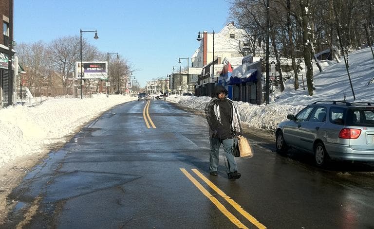 A woman walks down Washington St. in Dorchester, as the sidewalks are still covered in snow. (Delores Handy/WBUR)