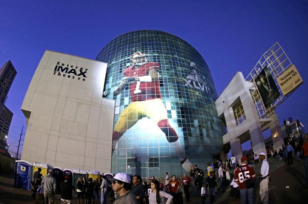 Super Bowl football fans walk past a several-stories tall likeness of San Francisco 49ers' Colin Kaepernick on the Audubon Nature Center along the Riverwalk, Saturday, Feb. 2, 2013, in New Orleans.  (AP)