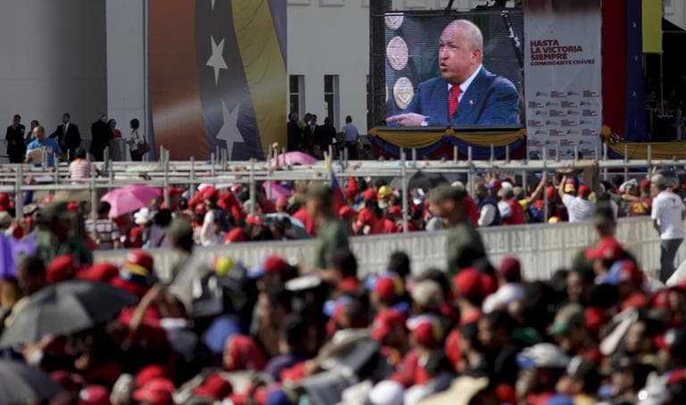 A screen showing a video image of Venezuela's President Hugo Chavez plays in front of the site where Chavez's funeral ceremony will take place as people gather outside the military academy in Caracas, Venezuela, Friday, March 8, 2013. (Ariana Cubillos/AP)