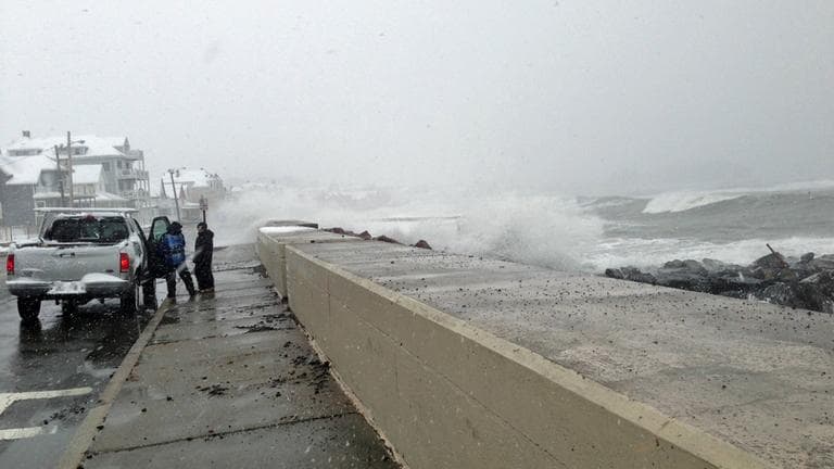 Waves breech the sea wall in Winthrop Friday morning as onlookers leave before they get wet. (Jesse Costa/WBUR)