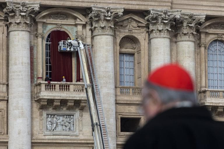 Cardinal Renato Martino walks by as workers use a crane to place a burgundy curtain around the door frame of the balcony on the front of St. Peter's Basilica on Monday, March 11, 2013, where the newly elected pope will make his first appearance to salute the cheering crowd. (Andrew Medichini/AP)