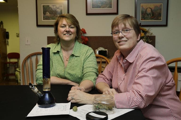 Married couple Kimberly Bliss, left, and Kim Ridgway, right, pose for a photo at their home in Lacey, Wash, in February 2013. On the table in front of them is medical marijuana and a water pipe that Ridgway uses to treat arthritis and severe anxiety. (Ted S. Warren/AP)