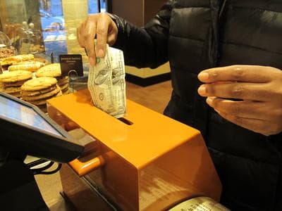 A customer inserts cash into a donation box to pay for her order at Panera Cares in Boston. (Kevin Sullivan/Here &amp; Now)