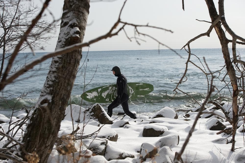 A surfer strides over ice covered rocks to reach the winter surf on Lake Superior. (Bob Tema)