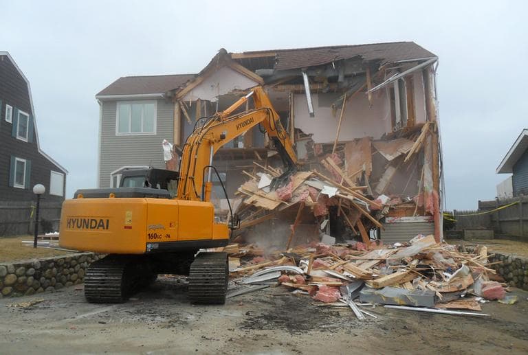 An excavator demolishes a home on Plum Island after the March storm. (Bruce Gellerman for WBUR)