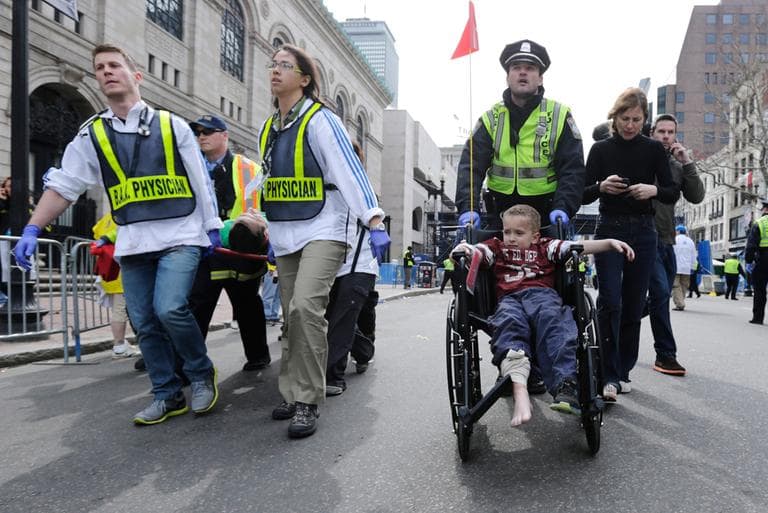A Boston police officer wheels in injured boy down Boylston Street as medical workers carry an injured runner following an explosion during the 2013 Boston Marathon in Boston, Monday, April 15, 2013. Two explosions shattered the euphoria at the marathon’s finish line on Monday, sending authorities out on the course to carry off the injured while the stragglers were rerouted away from the smoking site of the blasts. (Charles Krupa/AP)