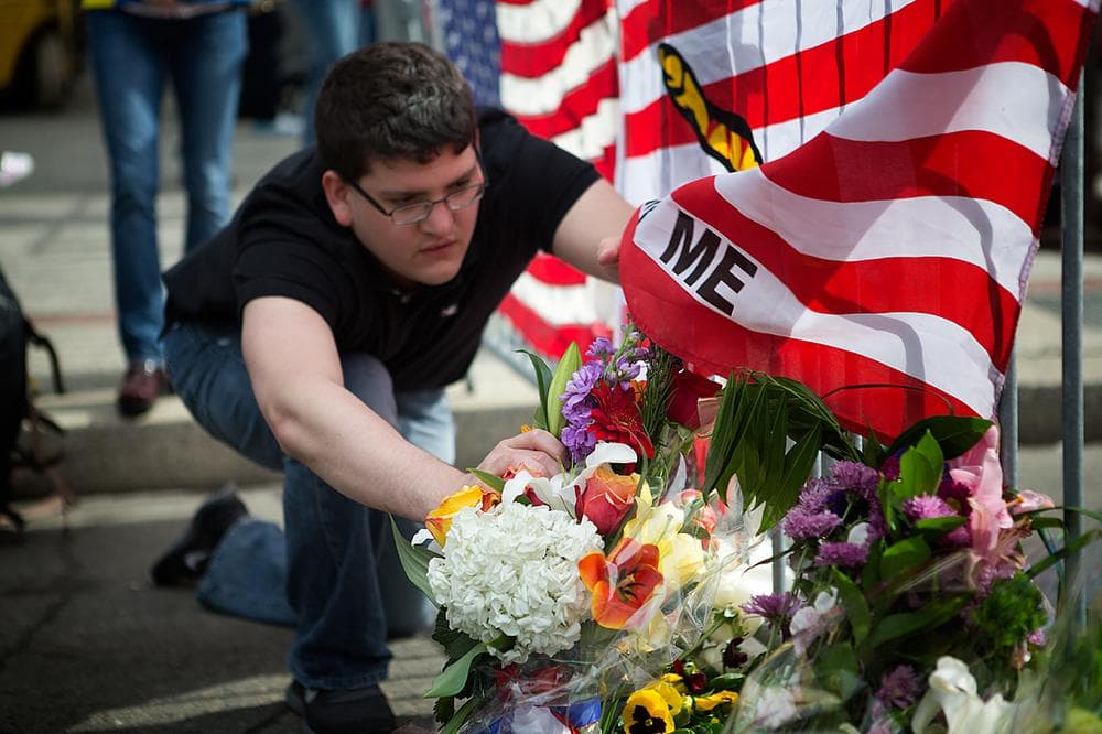 Leif Ruben of Back Bay props up flowers blown over by the wind at the Memorial at Clarendon and Boylston St. (Jesse Costa/WBUR)