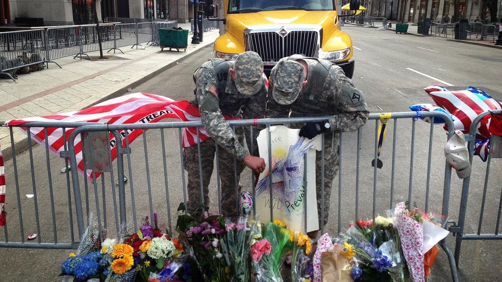 Two Army National Guardsmen adjust a poster that is part of a memorial set up on Clarendon Street. (Jesse Costa/WBUR)