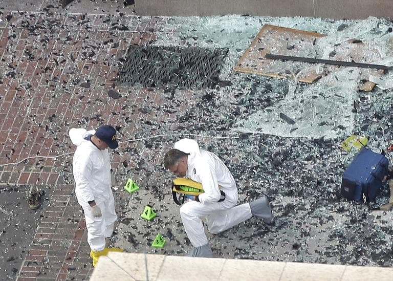Two men in hazardous materials suits put numbers on the shattered glass and debris as they investigate the scene at the first bombing on Boylston Street on Tuesday. (Elise Amendola/AP)