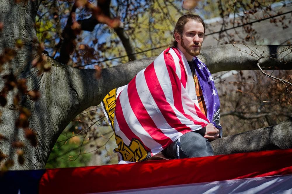Sitting in a tree, Devon Morancie of Littleton wears a flag as he watches the funeral procession arrive. (Jesse Costa/WBUR)