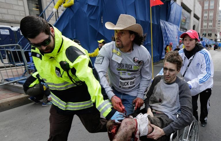 An emergency responder and volunteers push Jeff Bauman in a wheelchair after he was injured in an explosion near the finish line of the Boston Marathon on April 15. (Charles Krupa/AP)