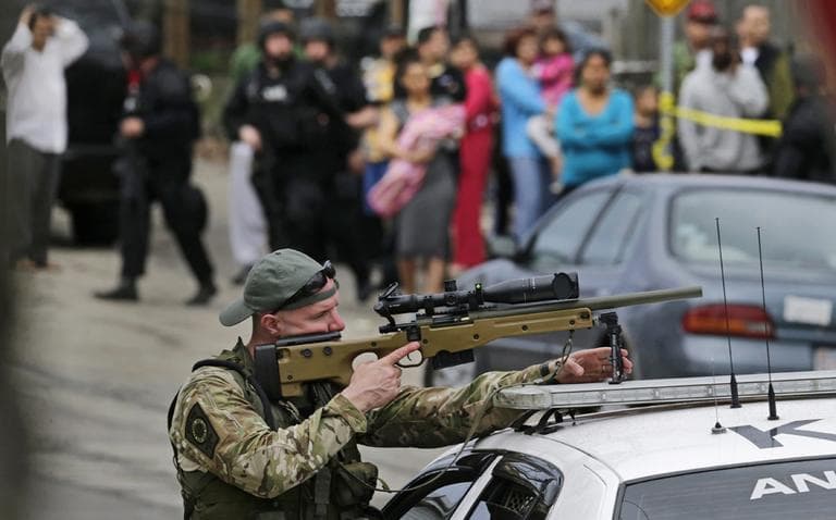 A sharpshooter trains his sight on a building as neighborhood residents stand on the street while police search for a suspect in the Boston Marathon bombings in Watertown, Friday, April 19. (Charles Krupa/AP)