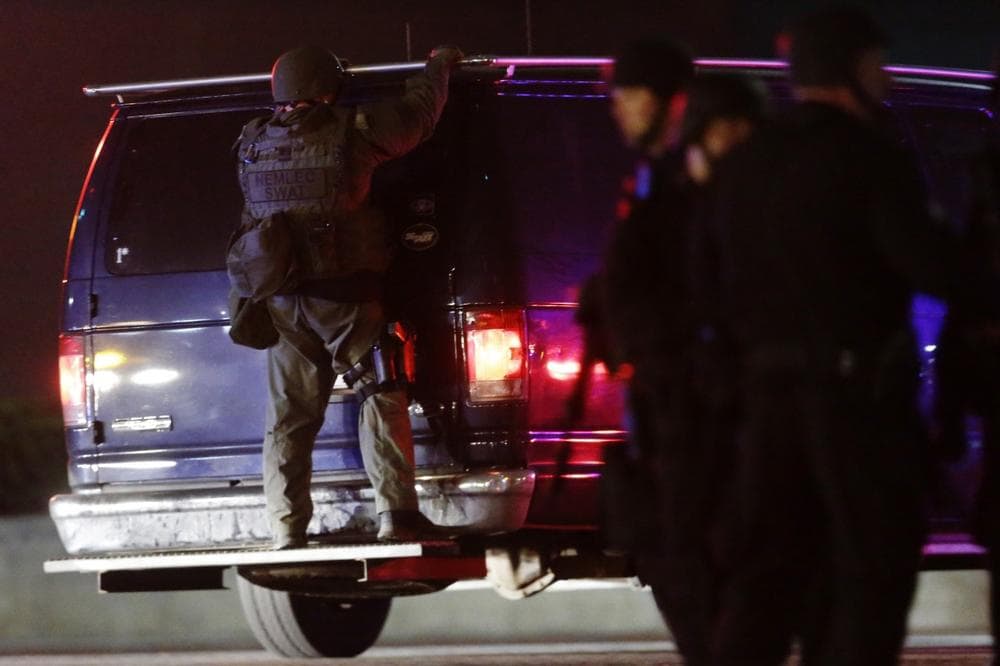 A police officers rides on the back of a van at a staging area as a manhunt is conducted for a suspect Friday, April 19, 2013, in Watertown, Mass. One of two suspects in the Boston Marathon bombing is dead and a massive manhunt is underway for another, authorities said early Friday April 19, 2013. Residents of Watertown, a Boston suburb, have been advised to keep their doors locked and not let anyone in.  (AP Photo/Matt Rourke)