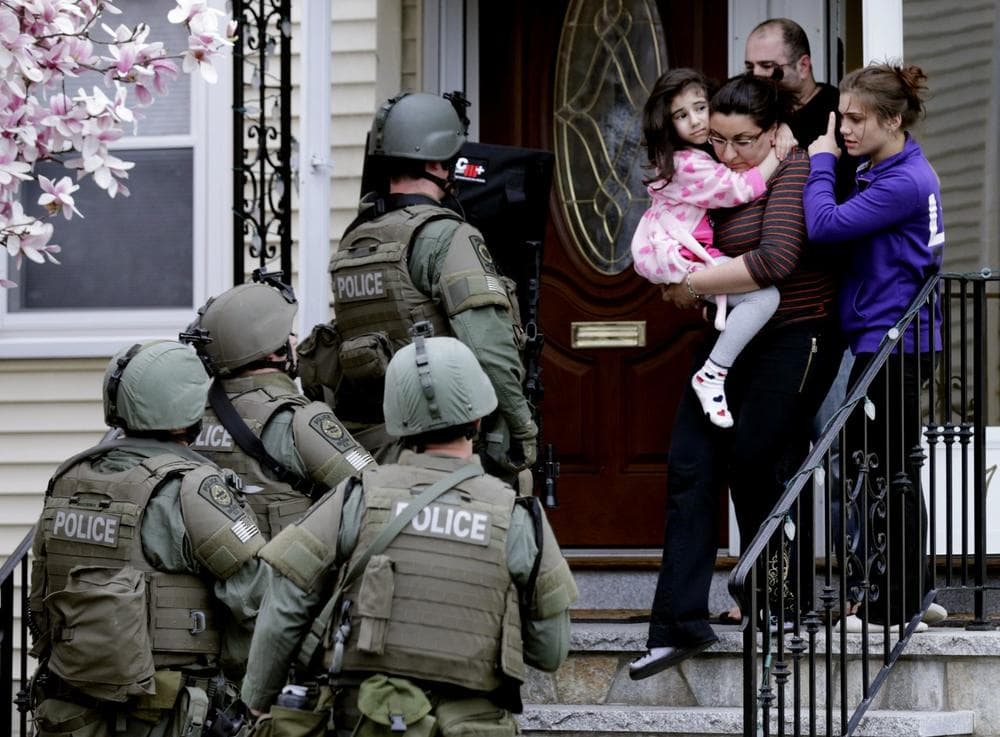 In this Friday, April 19, 2013 file photo, a woman carries a girl from their home as a SWAT team searching for a suspect in the Boston Marathon bombings enters the building in Watertown, Mass. Two suspects in the Boston Marathon bombing killed an MIT police officer, injured a transit officer in a firefight and threw explosive devices at police during their getaway attempt in a long night of violence that left one of them dead and another captured. Since Monday, Boston has experienced five days of fear, beginning with the marathon bombing attack, an intense manhunt and much uncertainty ending in the death of one suspect and the capture of the other. (AP Photo/Charles Krupa, File)