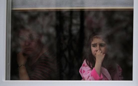 A girl looks out the window of her family’s home as a SWAT team drives through her neighborhood while searching for a suspect in the Boston Marathon bombings in Watertown, Mass., Friday, April 19, 2013. (AP Photo/Charles Krupa)