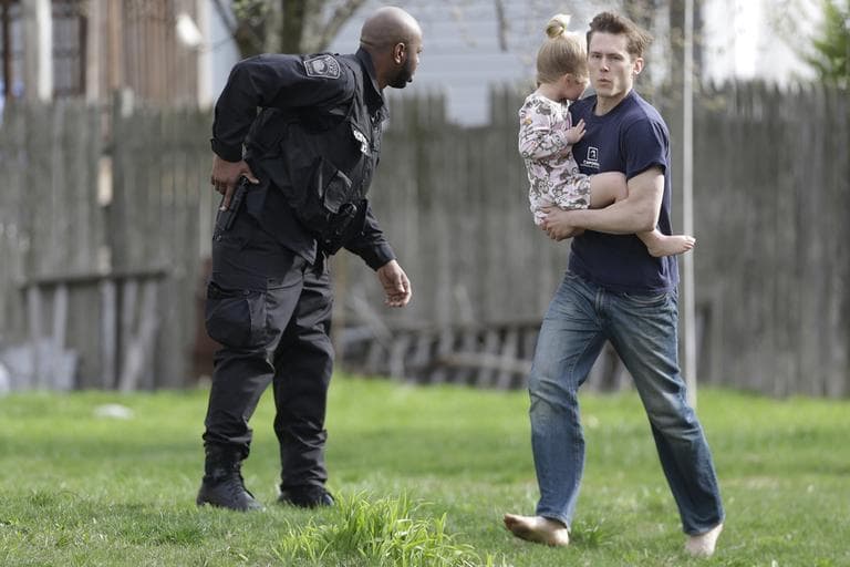 A police officer evacuates a shoeless man holding a child as members of law enforcement continue to search for the bombing suspect in Watertown Friday morning. (Matt Rourke/AP)