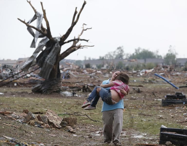 A woman carries her child through a field near the collapsed Plaza Towers Elementary School in Moore, Okla., Monday, May 20, 2013. (Sue Ogrocki/AP)