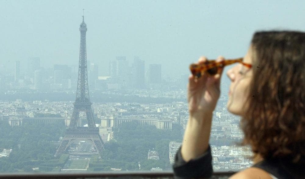 An unidentified woman puts on sunglasses as she looks at the Eiffel Tower under a heat haze in Paris, August, 2003. (Franck Prevel/AP)