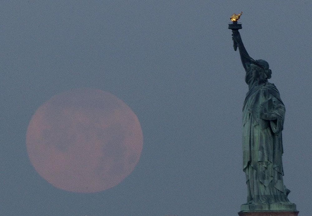 The supermoon sets near the Statue of Liberty. (Julio Cortez/ AP)