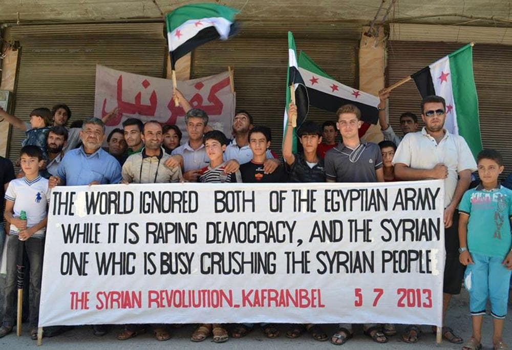 This citizen journalism image provided by Edlib News Network, ENN,  shows anti-Syrian regime protesters holding a banner and Syrian revolution flags during a demonstration at Kafr Nabil town in Idlib province, northern Syria, Friday. (AP/Edlib News Network ENN)