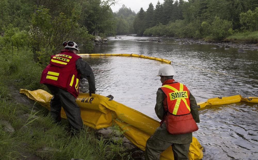 Environment workers lay booms on the Chaudiere River near Lac-Megantic, Que., to contain the crude oil spill following a train derailment and explosion, Tuesday, July 9, 2013. (Jacques Boissinot/The Canadian Press via AP)