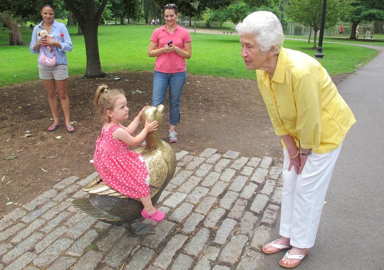 Nancy Schon talks to a little visitor climbing on the ducks. (Andrea Shea/WBUR)