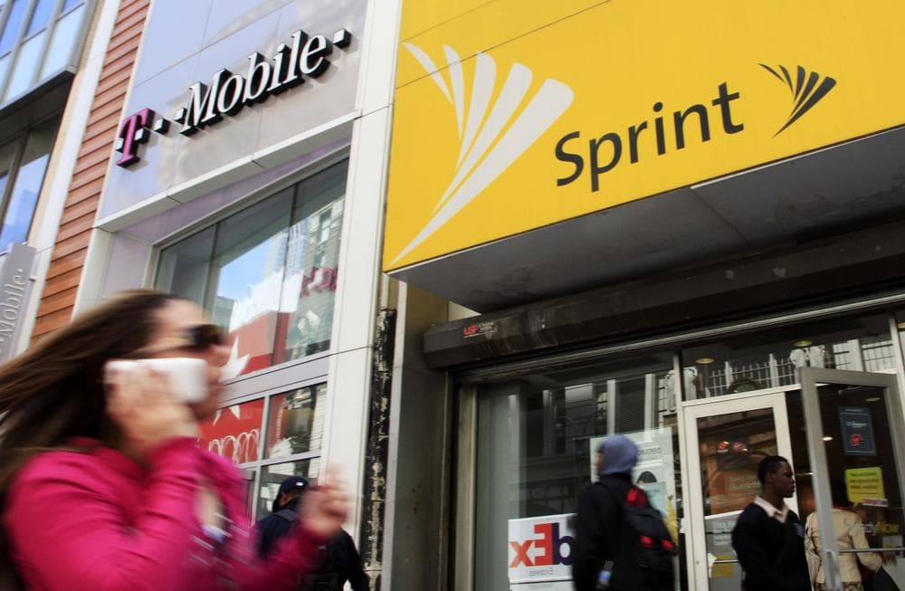 A woman using a cell phone walks past T-Mobile and Sprint stores in New York. Sprint and T-Mobile are eating into AT&amp;T and Verizon's consumer bases. (Mark Lennihan/AP)