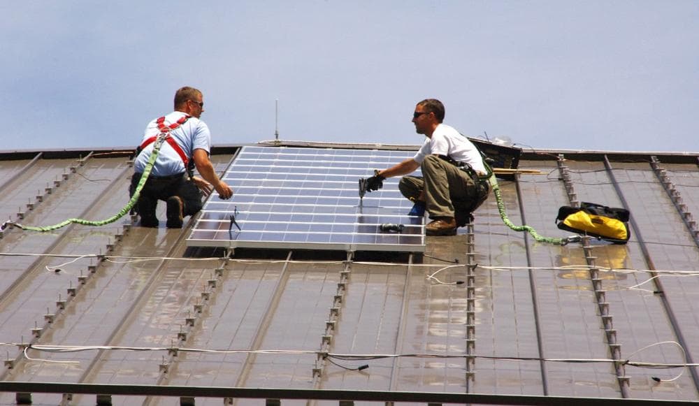Two workers install solar panels on a rooftop in Fort Dix, Texas. (U.S. Army Environmental Command/Flickr)