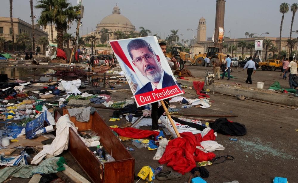 An Egyptian carries a poster of Egypt's ousted President Mohammed Morsi among debris from a protest camp in Nahda Square, Giza, Cairo, Egypt, Thursday, Aug. 15, 2013. (Amr Nabil/AP)