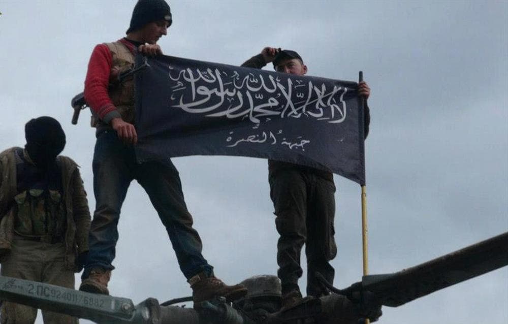 This Jan. 11, 2013 citizen journalism image shows rebels from al-Qaida affiliated Jabhat al-Nusra waving their brigade flag as they stand on a Syrian air force helicopter, at Taftanaz air base that was captured by the rebels, in Idlib province, northern Syria. (Edlib News Network ENN via AP)