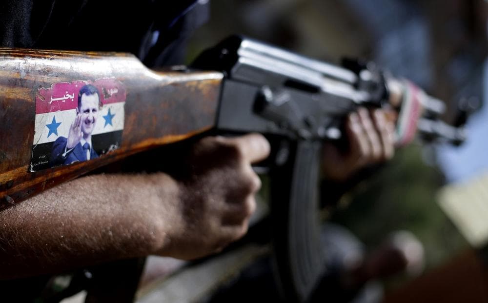 A Syrian military soldier holds his Ak-47 with a sticker of Syrian President Bashar Assad and Arabic that reads, &quot;Syria is fine,&quot; as he stands guard at a check point in Damascus, Syria, Wednesday, Aug. 21, 2013. (Hassan Ammar/AP)