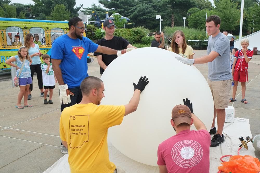 SLU students Joseph Wilkins, Patrick Walsh, Jackie Ringhausen and Tim Barbeau (standing, from left to right), and Valparaiso Univ. trainers Alex Kotsakis and Mark Spychala (crouching, left to right) stabilize the balloon as it fills with helium. (Art Chimes/St. Louis Public Radio)