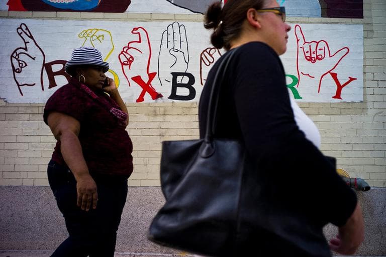Pedestrians walk past one of several murals along Ruggles Street near Dudley Square. (Dominick Reuter for WBUR)