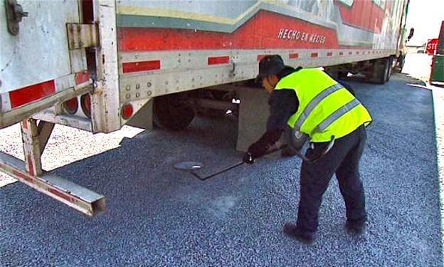 At a truck yard in Otay Mesa, a security guard checks for drugs hidden underneath a truck. Smugglers have been known to attach drugs to the underside of vehicles with powerful magnets.(Roland Lizarondo/Fronteras Desk)