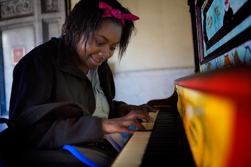 A curious Medina Phillips, 22, plays the piano outside the Strand Theater. (Jesse Costa/WBUR)