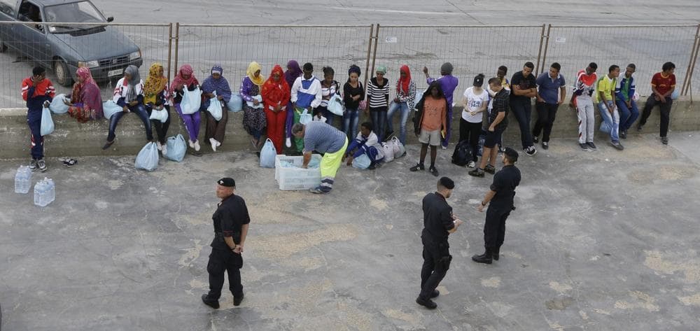 Carabinieri paramilitary police officers look at migrants waiting to board a ferry boat from the port of Lampedusa, for Sicily, southern Italy, where they will be sent to other temporary camps based on their legal status, Monday, Oct. 7, 2013 (AP/Luca Bruno)