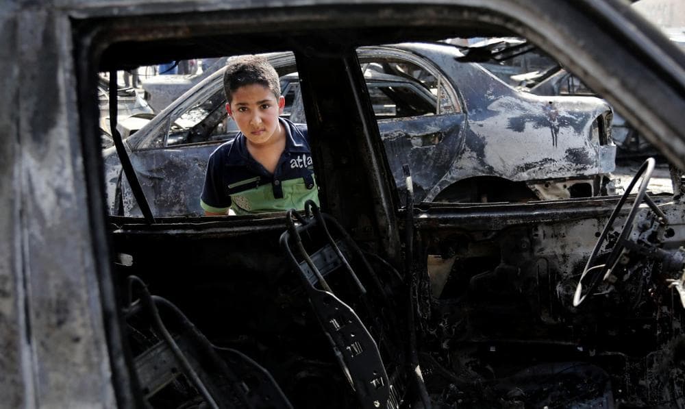A boy inspects a destroyed car after a car bomb attack hit the Sha'ab neighborhood of Baghdad, Iraq, Sunday, Oct. 27, 2013. (Karim Kadim/AP)
