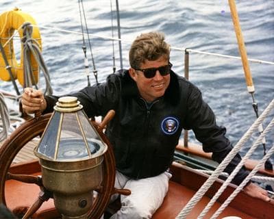 President John F. Kennedy sits at the helm of the United States Coast Guard boat &quot;Manitou&quot; while sailing off the coast of Johns Island, Maine. (Courtesy JFK Library)