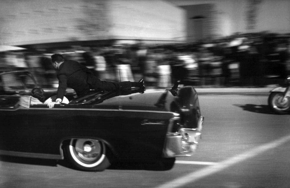 The limousine carrying mortally wounded President John F. Kennedy races toward the hospital seconds after he was shot in Dallas, Tx., Nov. 22, 1963. With secret service agent Clinton Hill riding on the back of the car, Mrs. John Connally, wife of the Texas governor, bends over her wounded husband, and Mrs. Kennedy leans over the president. (Justin Newman/AP)