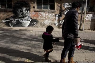 A woman leads a child while holding a doll as they walk near mural depicting a child eating in Beijing Sunday, Nov. 17, 2013. Experts estimate that the first easing of the country's strict one-child policy in three decades announced this month allowing couples where one partner is an only child to have a second baby will result in 1 million to 2 million extra births per year in the first few years, on top of the 16 million babies born annually in China. (AP)