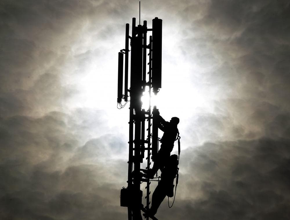 Two workers are silhouetted as they fix a mobile phone pole against the sun. (AP)