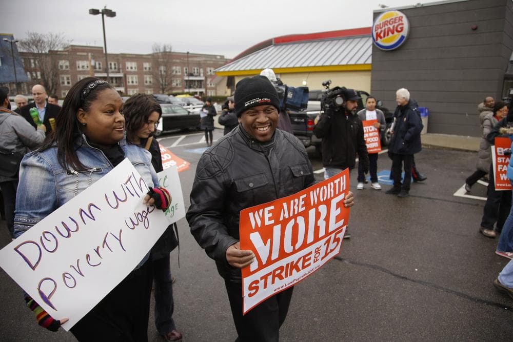 Kilra Hilton, left, and Kyle King talk while they march participating in a demonstration on a Burger King parking lot as part of a nation-wide protest supporting higher wages for workers in the fast-food industry and other minimum wage jobs in Boston, Thursday, Dec. 5, 2013. (Credit: AP/Stephan Savoia)