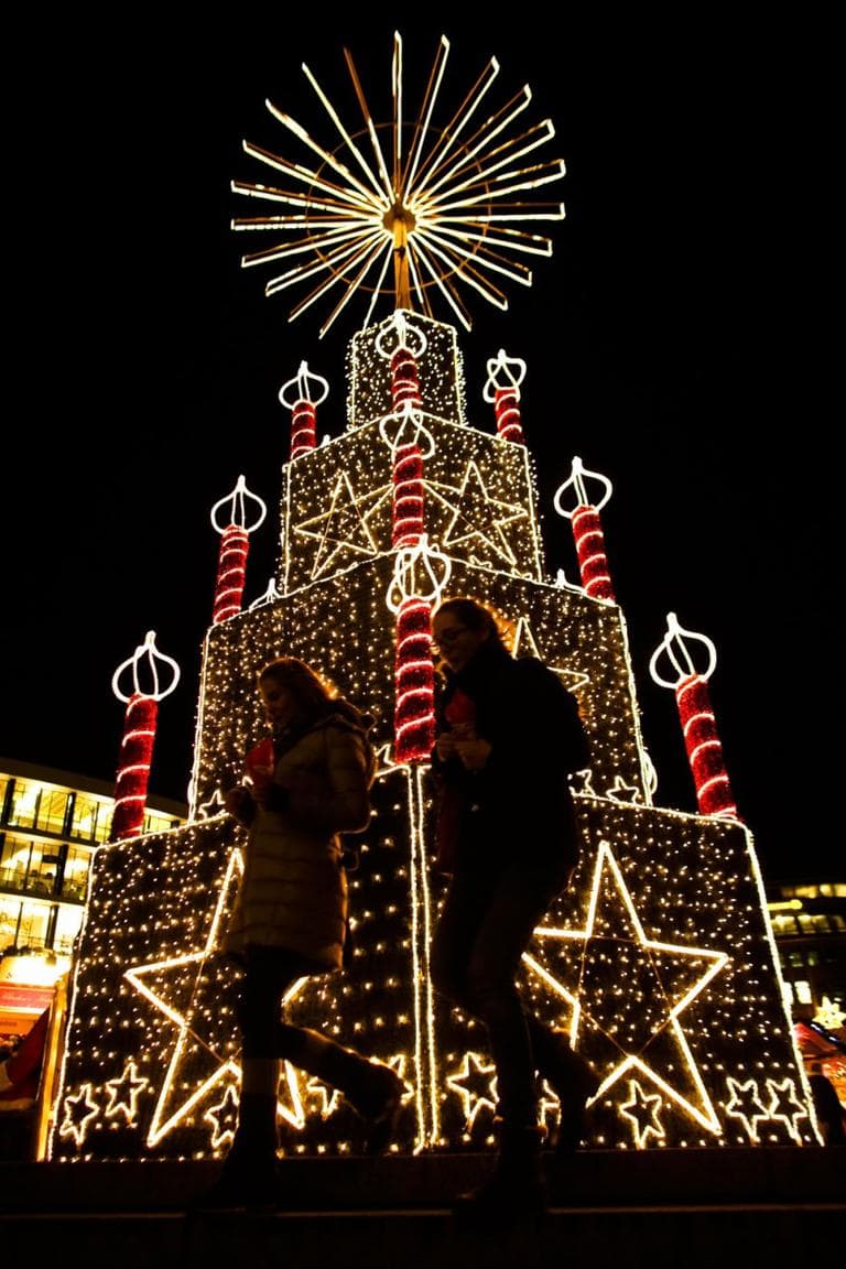 Two women walk in front of a Christmas illumination at the Christmas market at Breitscheid Place in Berlin, Germany, on Nov. 25, 2013. The opening of the markets in Berlin signifies the start of the 2013 Christmas season. (AP Photo/Markus Schreiber)